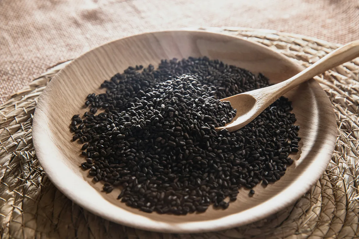 Black glutinous rice grains poured from a wooden scoop onto a rustic surface, showing their deep purple-black colour